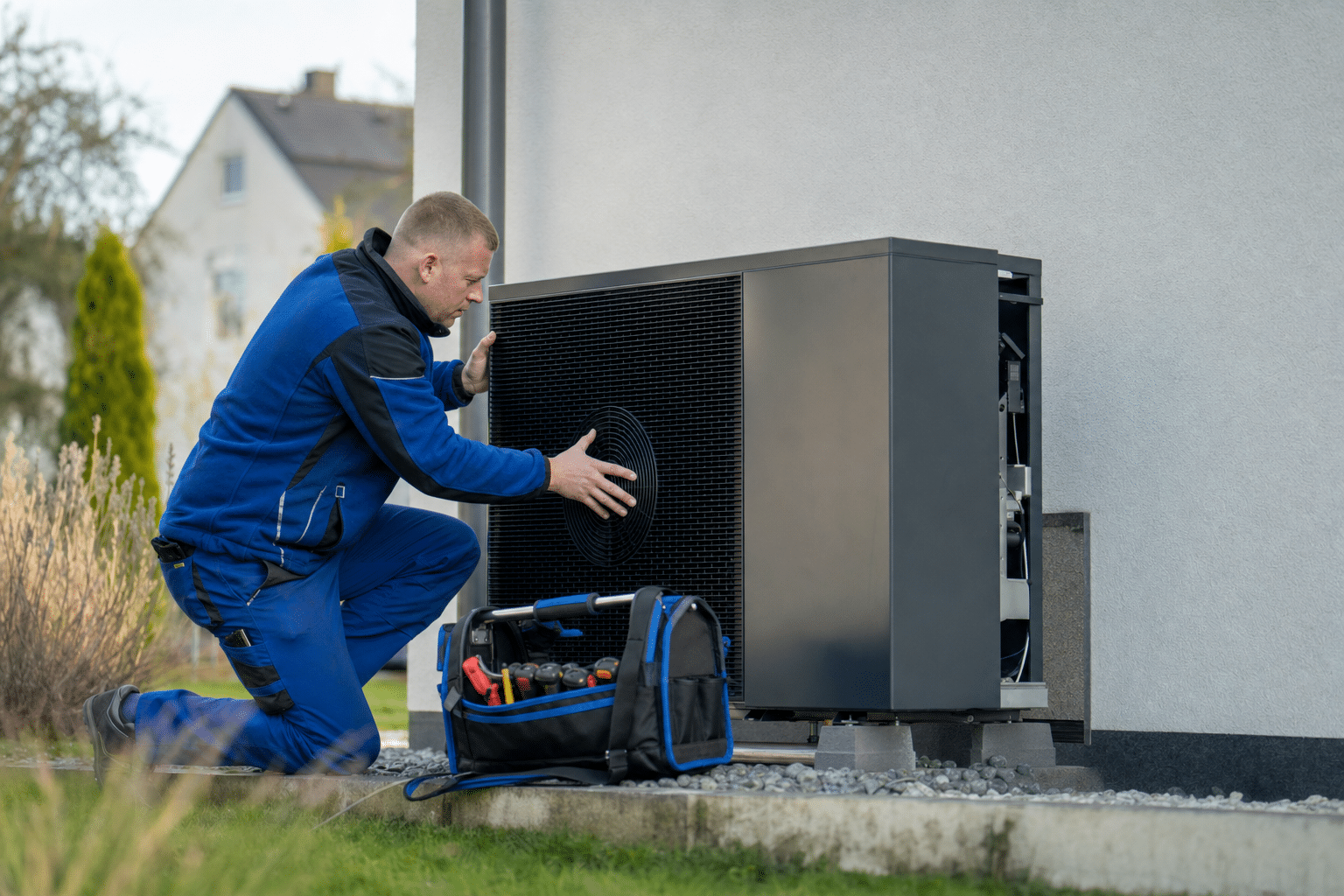 Installateur montiert eine moderne Wärmepumpe neben einem Einfamilienhaus