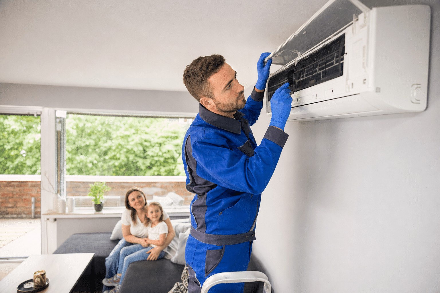 Servicetechniker reinigt das Innengerät einer Klimaanlage in einem bewohnten Wohnzimmer